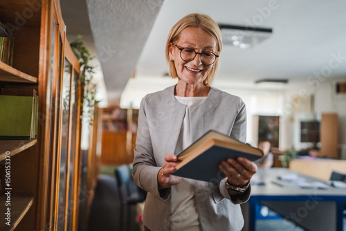 smile mature woman teacher read a book in the library photo