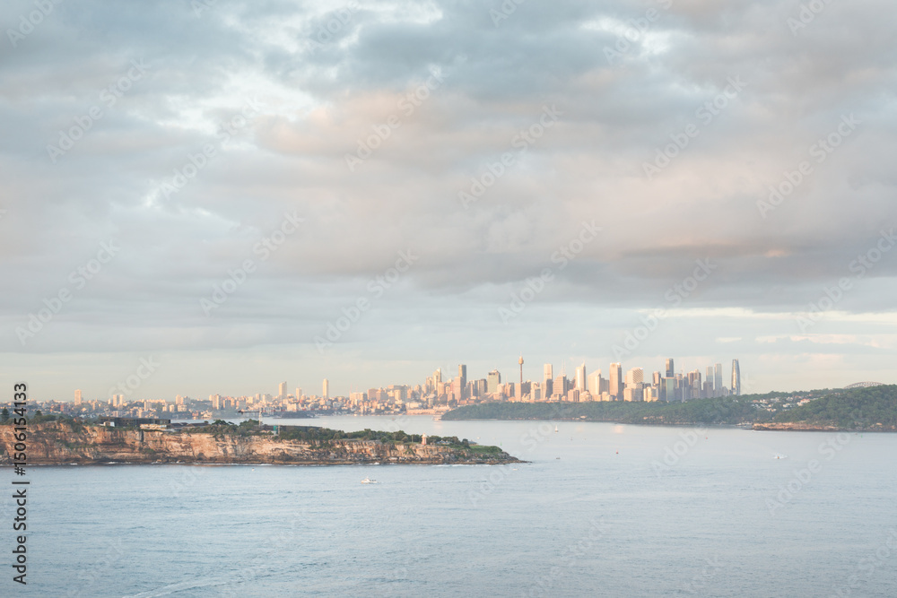 Fototapeta premium Early morning view of Sydney skyline from Burragula Lookout, North Head. Ocean in foreground, city in background, sunlit clouds in the sky create a moody atmosphere.