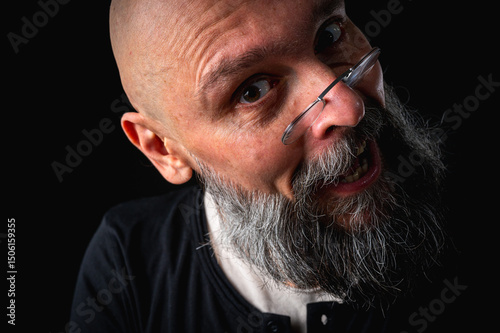 Funny close-up portrait of a quirky bald man with a long gray beard and eyeglasses, making a silly face. Concept of eccentricity, humor, and expressive personality.