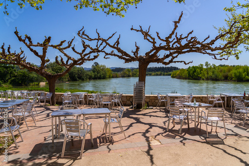 Outdoor cafe seating area overlooking a river on a sunny day.