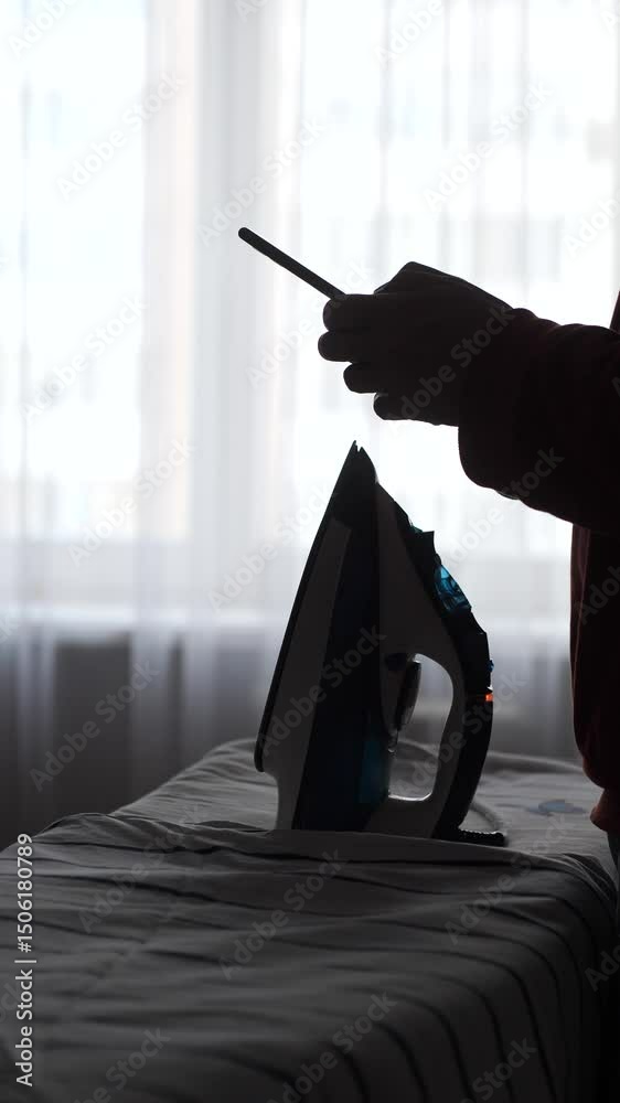 vertical video Silhouette of person using smartphone near ironing board