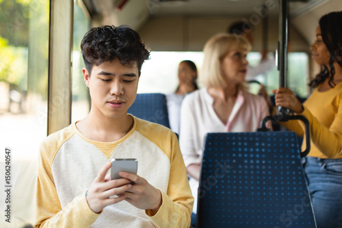 Фотография Portrait of young Asian guy traveling on public transit and using cellphone sitt