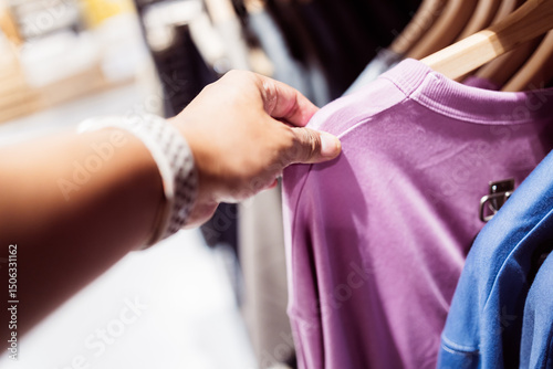 Fotografia Person is having shopping experience by touching purple shirt on retail display