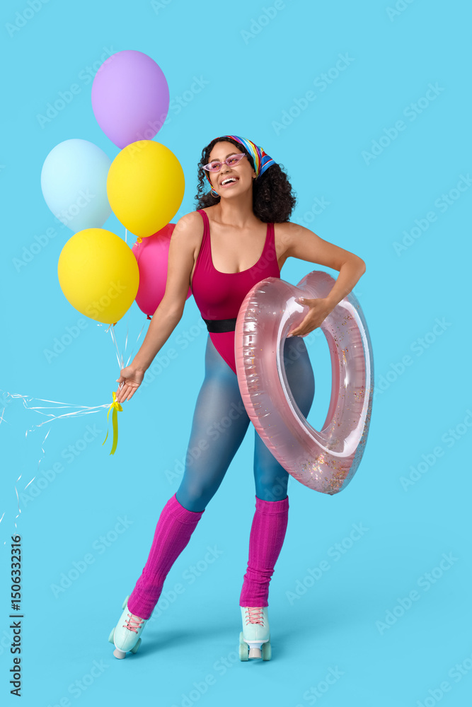 Young African-American woman in roller skates with swim ring and balloons on blue background. Summer party Young African-American woman in roller skates with swim ring and balloons on blue background. Summer party