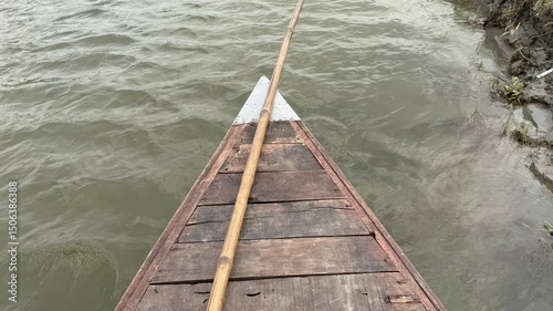 Fototapeta Naklejka Na Ścianę i Meble -  Bamboo pole rests on the old wooden boat's front as it navigates river