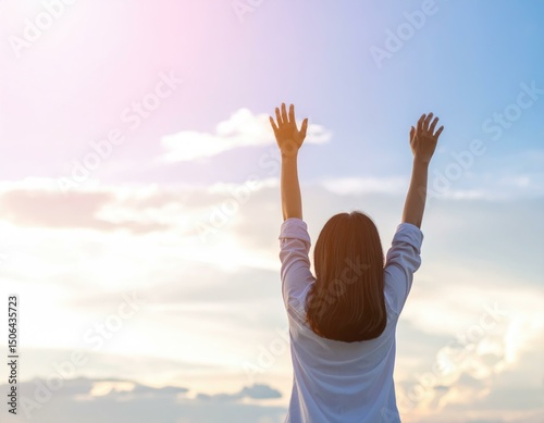 Woman raising arms towards sunset sky, feeling freedom and hope. Image depicts peace, serenity, and gratitude.
