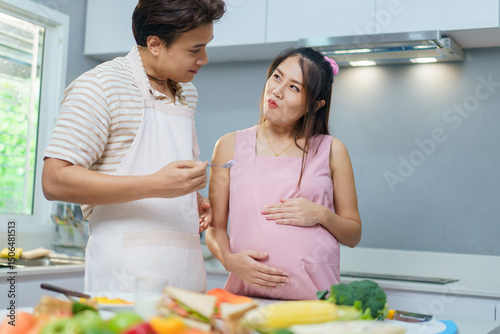 Asian couple, with the wife heavily pregnant, happily preparing food and peeling fruit together in the kitchen. 