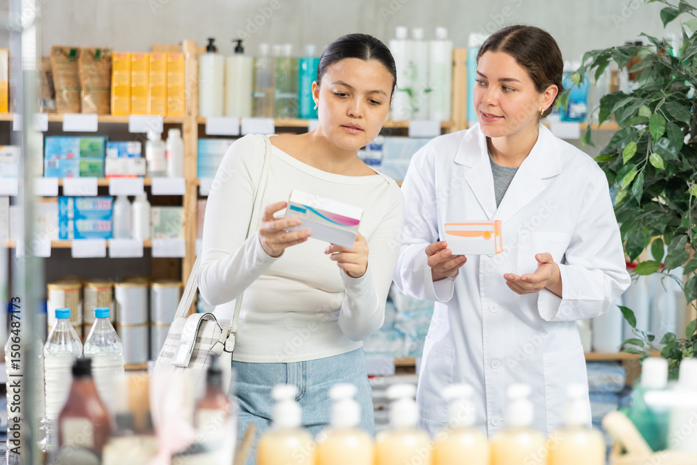 Obraz premium Portrait of young woman pharmacist helping asian female client choosing pill box and making decisions about pharmaceuticals and health care at modern pharmacy