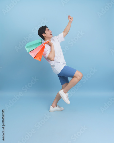 Young man joyfully celebrates shopping with colorful bags against a blue background