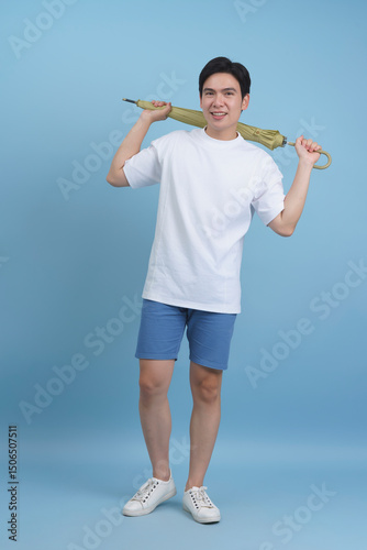 Young man holding an umbrella with a cheerful smile in a light blue background during a studio photoshoot
