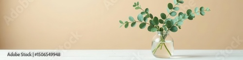 Stylish eucalyptus arrangement in clear glass vase, white wood table, beige backdrop , stock, branding