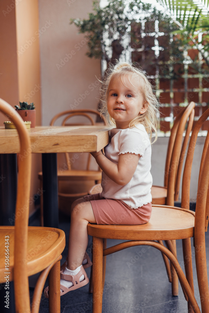 Child smiles while seated at wooden chair in modern cafe Child smiles while seated at wooden chair in modern cafe