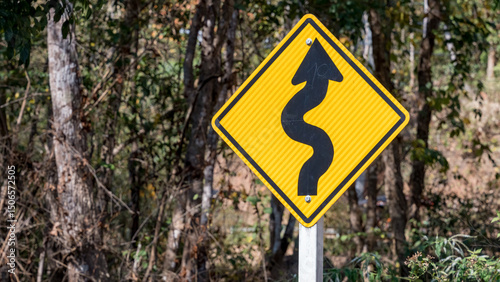 Winding road warning sign in forest area with arrow curve symbol