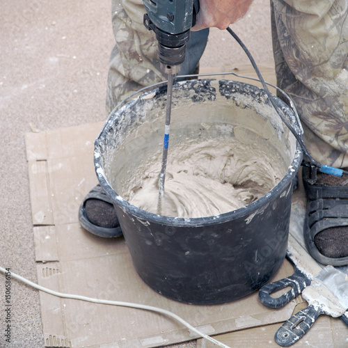 A worker stirs the construction mixture plaster in a bucket with an electric stirrer.