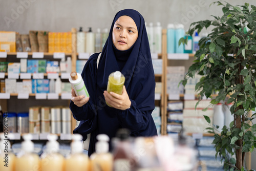 Foto Thoughtful young Asian woman in navy blue chador and abaya examining shampoo bot