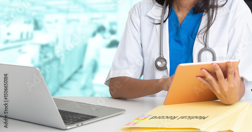Female doctor working with digital tablet and laptop at desk in hospital.