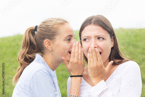 Blond woman gossiping in female friend's ear in nature photo