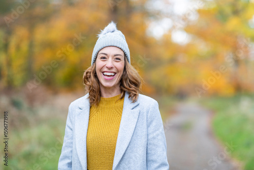 Cheerful woman wearing knit hat and jacket smiling while standing in forest