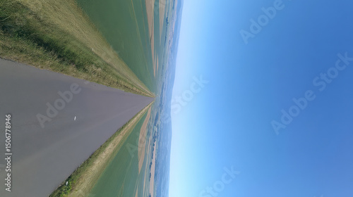 Wide road into distance, flanked by green fields and blue sky. High-definition, horizontal composition. Serene beauty.