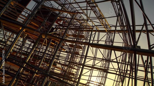 Wallpaper Mural Metallic scaffolding casting geometric shadows, backlit by vibrant sunset hues spreading across evening horizon Torontodigital.ca