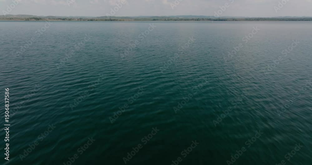 Slow upward drone tilt reveals the tranquil waters and distant shoreline of Lake Petén Itzá, Guatemala.