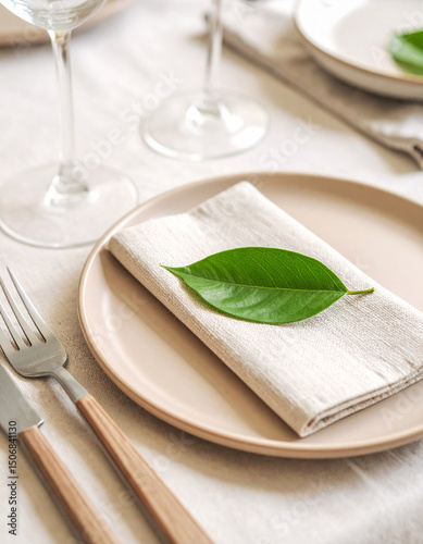 A solitary green leaf resting on a matte beige plate placed on a linen napkin.