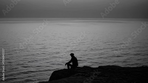 Contemplative silhouette at dusk: serene ocean view and reflective moment on cliff edge