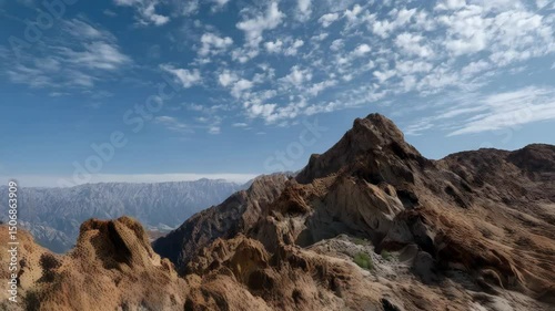 Sweeping landscape with rugged desert mountains and a vast blue sky filled with soft, cottony clouds during a sunny day.