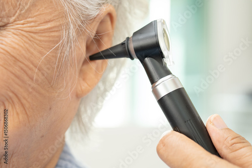 Audiologist or ENT doctor use otoscope checking ear of asian senior woman patient treating hearing loss problem.