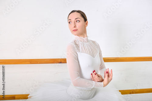 Foto Young female ballerina with dark hair in white costume poses gracefully in bright studio
