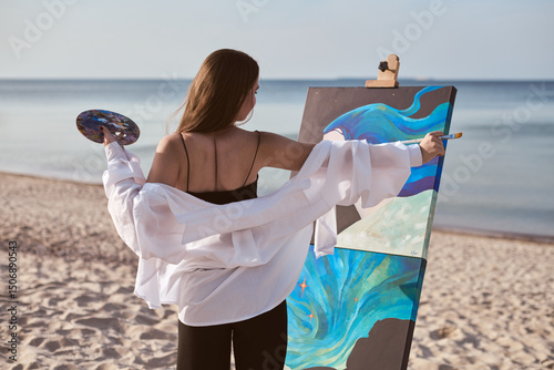 Young female painter stands by sea, absorbed in creating vibrant artwork on canvas. Beach setting and gentle waves add serenity, enhancing her creative expression