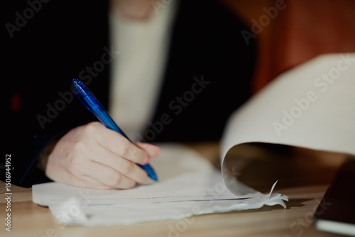 A professional reviewing multiple pages of documents on a wooden desk in a corporate environment.
