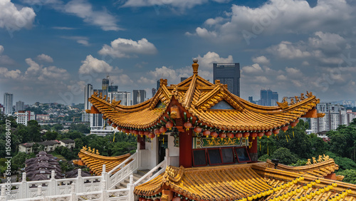 A beautiful Chinese temple against the skyscrapers of a modern city. A pagoda with a tiled roof. Rows of red, yellow lanterns along the curved edges of the cornices. Staircase, carved stone handrails