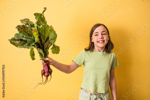 Little girl with fresh beetroot with leaves stands in front of a yellow wall. Organic food concept.