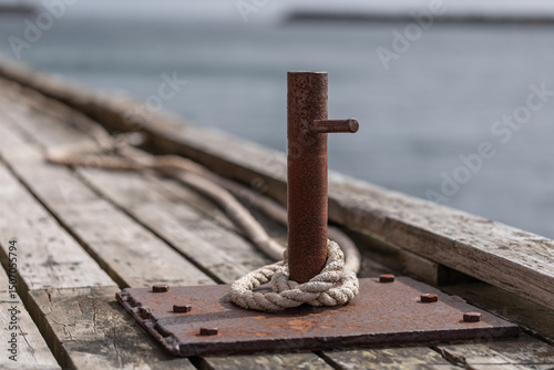 Foto Rusty mooring post with rope on old wooden pier by the sea