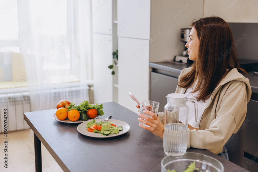 Young Woman Enjoying Healthy Meal and Browsing Smartphone in Modern Kitchen Young Woman Enjoying Healthy Meal and Browsing Smartphone in Modern Kitchen