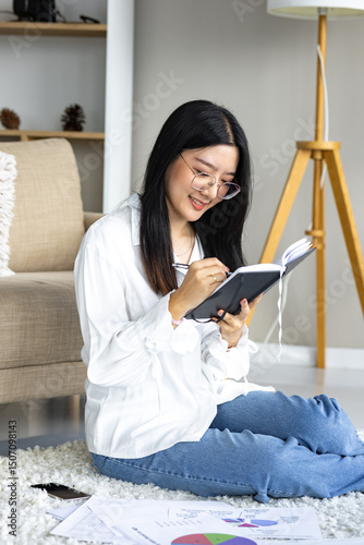 Casual woman reading a notebook while sitting on a carpet at home