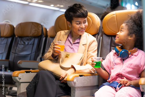 Passenger : African American daughter and mother  traveling by airplane. serving drinks.  Female steward serving glass of water for passengers on board. Flight attendant  and Cart on airplane