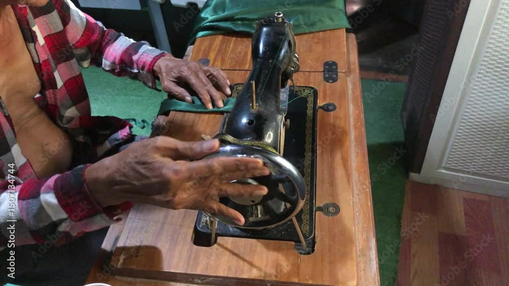 elderly man is sewing a garment with a manually operated, old-fashioned sewing machine