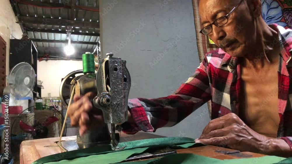 elderly man is sewing a garment with a manually operated, old-fashioned sewing machine