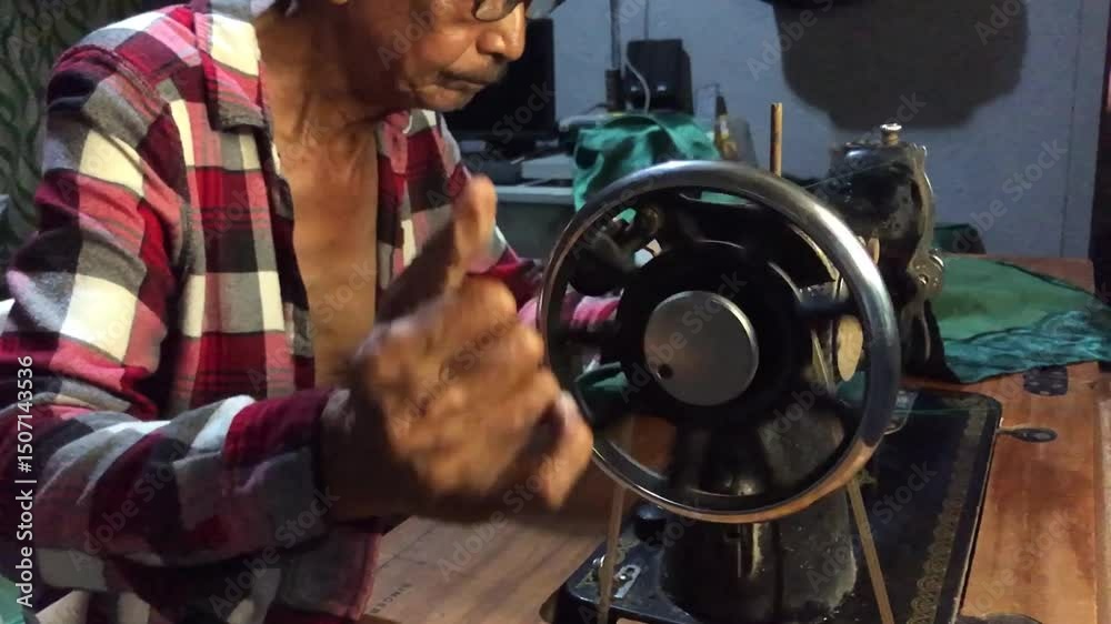 elderly man is sewing a garment with a manually operated, old-fashioned sewing machine