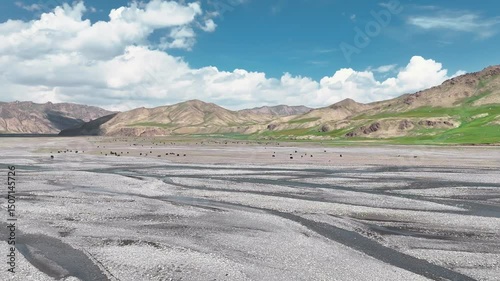 The winding river flows smoothly between the green hills, sparkling in the sun. Densely forested mountains rise all around, creating a picturesque landscape.