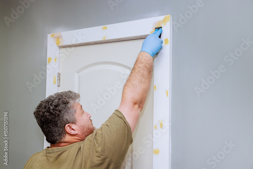Homeowner works applies wood filler on door trim, using tool while preparing before painting