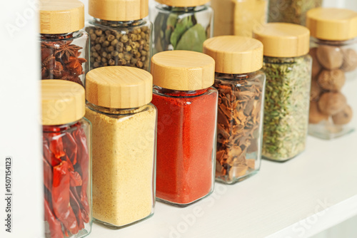 Many different aromatic spices in jars on white shelf indoors, closeup