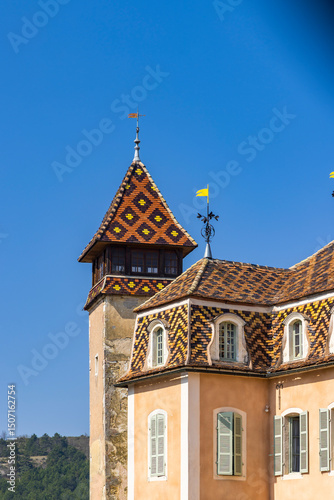 Colorful glazed tile roof and tower of Chateau de Monthelie in Burgundy, France, shining under blue sky