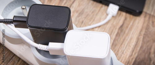 Black smartphone and chargers connected to electrical power strip. Various devices charging concept