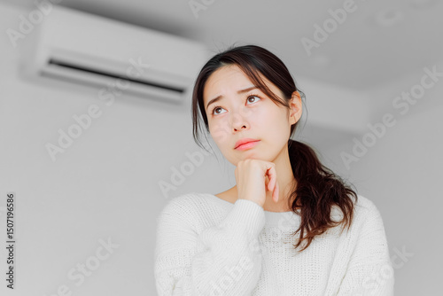 エアコンの故障で修理か買い替えかで悩む若い女性の表情