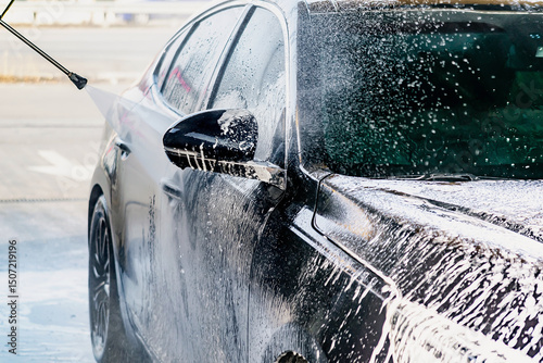 Driver washing car with contactless high pressure water jet,equipment pump in self service car wash.Vehicle covered with foam chemical detergents