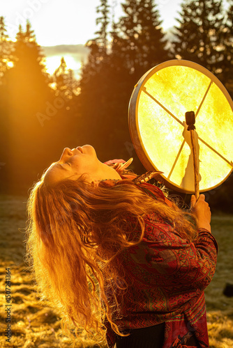 Beautiful shamanic girl playing on shaman frame drum in the nature.