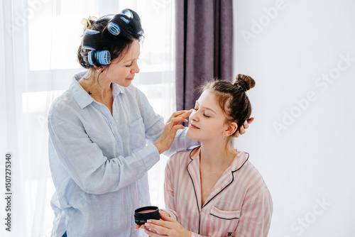Mom with hair rollers holding eye patch while smiling at teenage daughter photo
